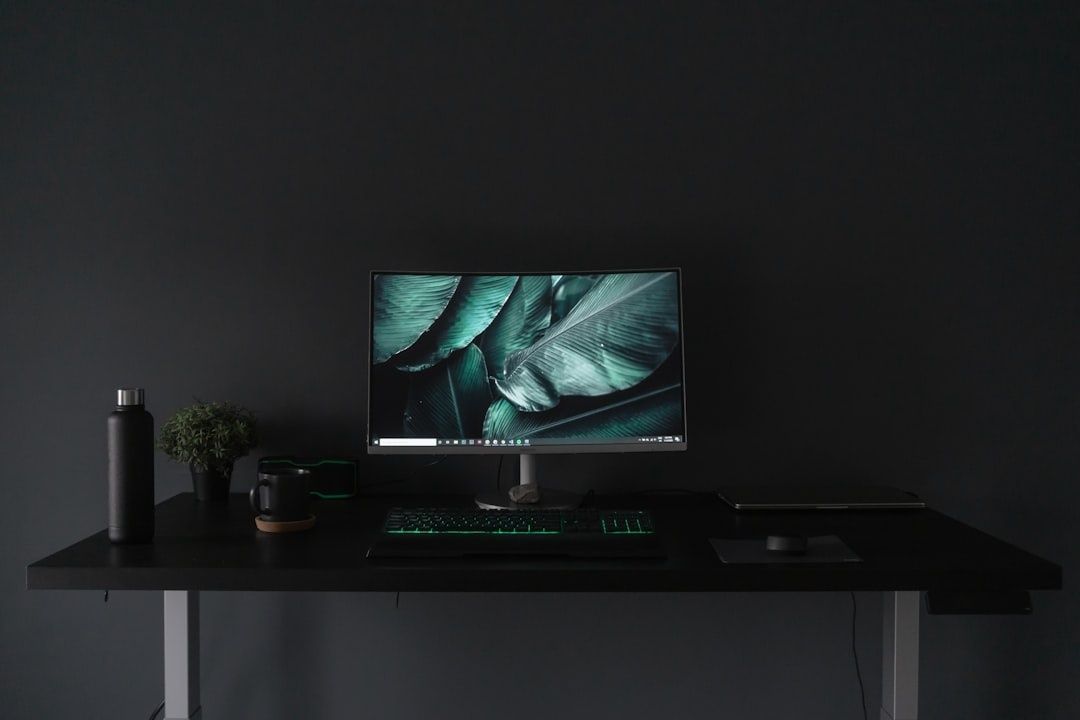 Mörkt skrivbord med datorskärm, tangentbord och växt